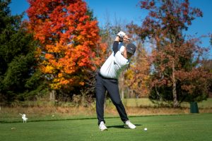 man swinging a golf club with autumn trees in the background